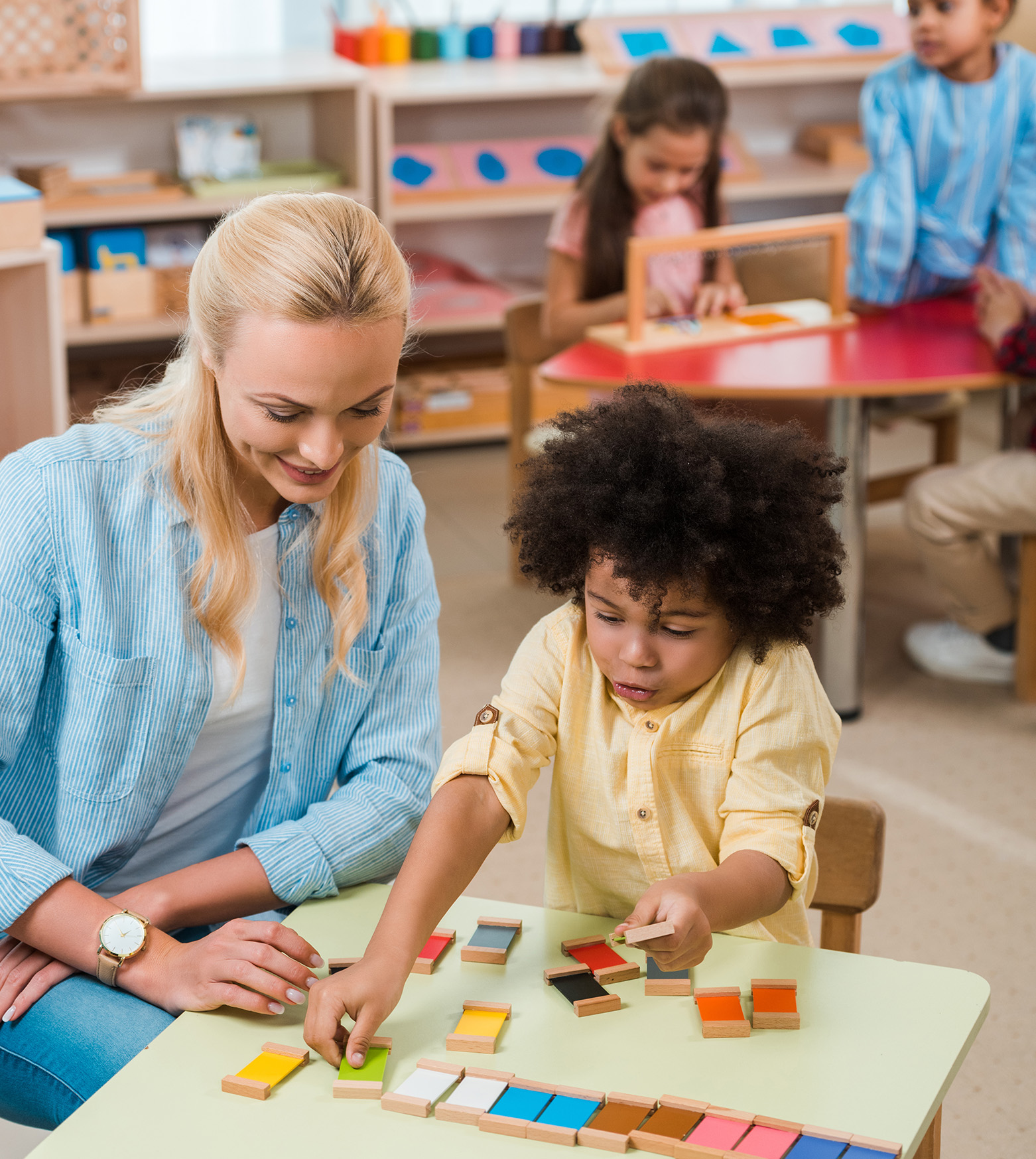 child playing game next to smiling teacher with kids at background in home daycare facility